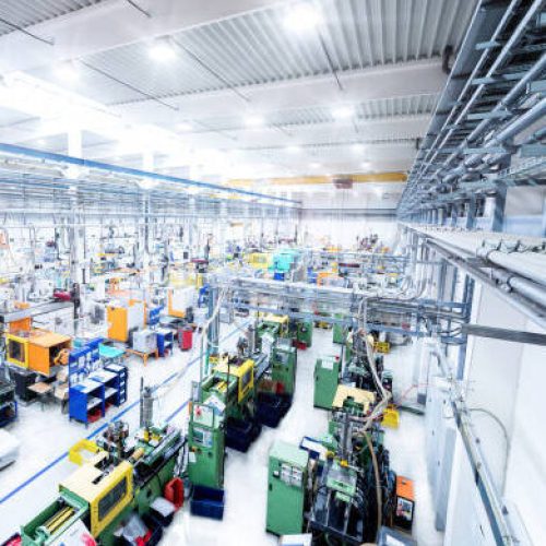 Horizontal high angle view color image of futuristic factory. Industrial aisle surrounded by modern machines which having busy robotic arms with molding shapes and producing plastic pieces for variety of industry. Labor intensive production line with manufacturing equipment - boxes, crates, crane, packages, pallets, space for copy